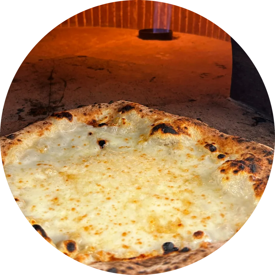 Pizza bianca appena sfornata, col cornicione bruciacchiato; dietro, la volta di mattoni del forno con la fiamma accesa