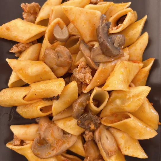 Pasta corta con salsiccia sbriciolata e funghi, su un piatto scuro