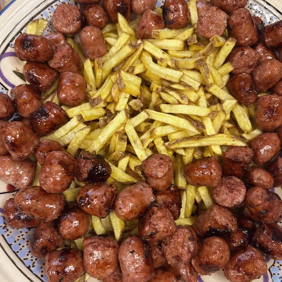 Salsiccia a tocchetti e patatine fritte in un piatto di ceramica decorato